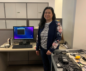 Mimi standing in front of a Linux preservation workstation, next to a cart with a variety of drives and cables on it