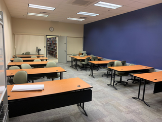 A room with computer tables and one dark blue wall. Through an open door bookshelves can be seen